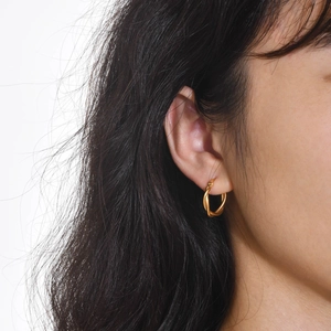 Close-up of elegant gold twisted hoop earrings worn by a model in a minimalist style