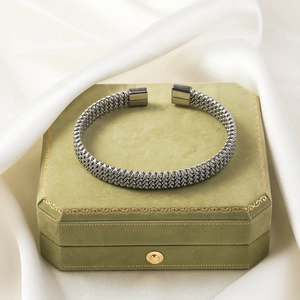 Macro shot of silver woven titanium steel cuff bracelet on green velvet box