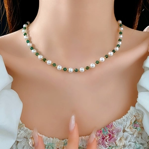 Detail of beaded necklace featuring white pearls and green gemstones on a model