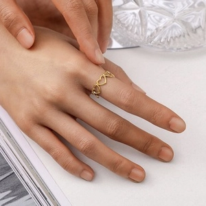 Detail of adjustable gold-plated heart link ring worn on index finger with sleek ripples