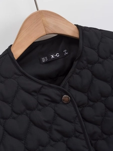 Detail of black heart-quilted jacket with metal snap button and brand neck label