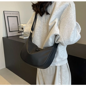 Detail of a black crescent crossbody bag in matte fabric worn by a model in casual style