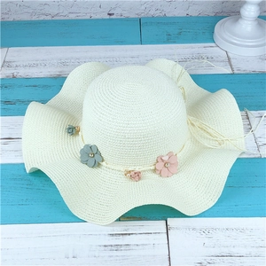 Détail d'un chapeau de paille beige clair avec bord ondulé et fleurs en tissu délicates