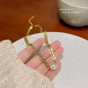 Baroque pearl necklace with gold wheat leaf chain elegantly held over a ceramic tray