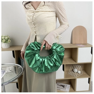 Detailansicht der smaragdgrünen Plissee-Handtasche mit rundem Griff in moderner Kulisse