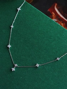 Macro shot of silver four-leaf clover necklace with sparkling cubic zirconia on green background
