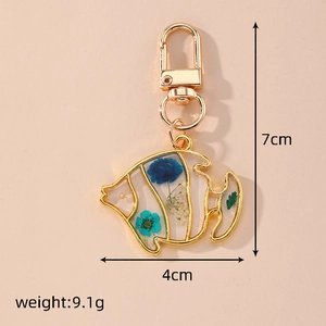 Detail of fish shape keychain with embedded blue dried flowers and golden frame