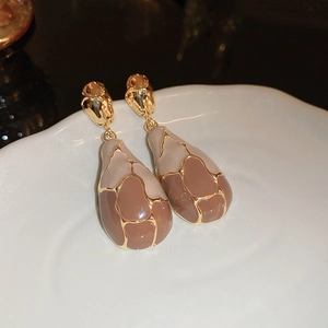 Detail of drop-shaped earrings with brown enamel and gold accents on ceramic tray