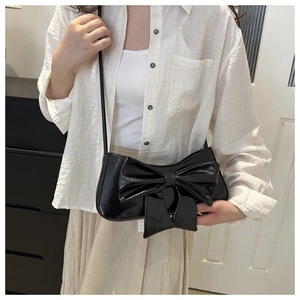 Detail of glossy black patent leather shoulder bag featuring a large decorative bow