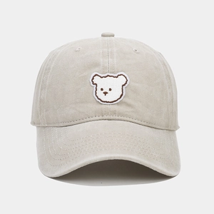 Close-up of the delicate white bear embroidery on the beige cotton baseball cap
