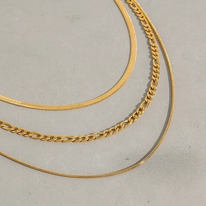 Detailed view of layered gold necklaces including snake chain and Figaro links