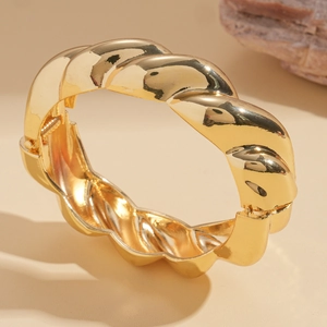 Detailed macro view of gold-tone chunky twisted bangle featuring a side hinge closure