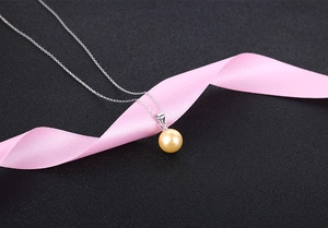 Detail shot of a champagne pearl pendant on a silver chain over pink silk ribbon