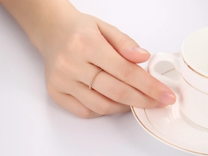 Detailansicht eines schmalen, gedrehten Rings in Roségold an einem Finger neben Kaffeetasse