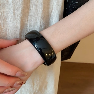 Bracelet manchette large en acrylique noir poli avec un style minimaliste rétro sur modèle