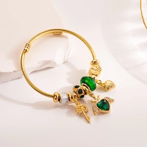 Gold adjustable bangle with green heart charm and cut glass beads on white stone