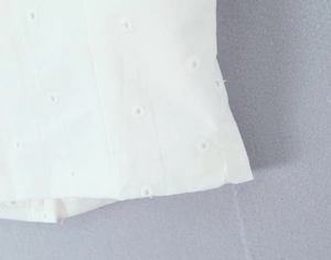 Detailed macro view of white cotton fabric featuring intricate eyelet embroidery patterns