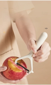 Close-up of sharp stainless steel Y-peeler peeling a red apple in a modern kitchen
