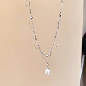 Collier double rang en argent avec pendentif perle élégant sur un fond beige neutre