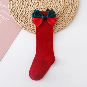 Detail of red Christmas baby socks with large green satin bow on a decorative mat