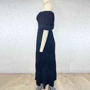Side view of black off-shoulder maxi dress with puff sleeves and layered cake skirt detail