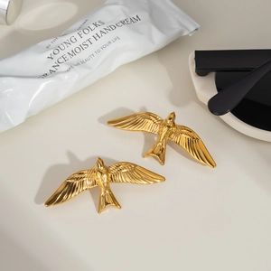 Vue détaillée de deux bijoux hirondelles dorés avec textures de plumes fines sur fond beige