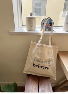 Detail of embroidered beloved lettering on beige canvas tote bag with soft natural lighting