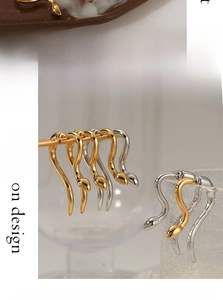 Macro detail of glossy gold and silver snake-shaped earrings on a creative display stand