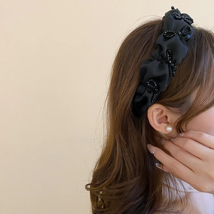 Vue détaillée d'un serre-tête en satin plissé noir orné de perles délicates et élégantes