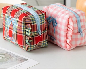 Detail of plaid makeup bags with embroidered bows and ruffle edges on white desk