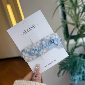 Close-up of blue plaid fabric hair clip with Orchid embroidery and bow on display card