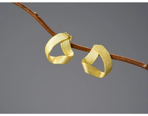 Macro view of gold matte twisted triangle silver earrings hanging on a tree branch