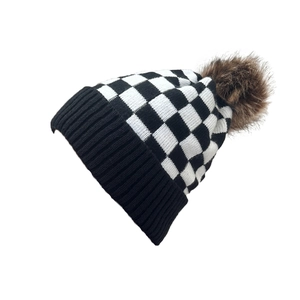 Detail of checkered knit beanie with a fluffy faux fur pom pom on white background