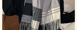 Detail shot of the thick plaid scarf showing soft texture and tassels in a home setting
