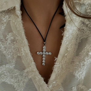Close-up of the large 18k gold cross pendant with zircons on a black cord necklace