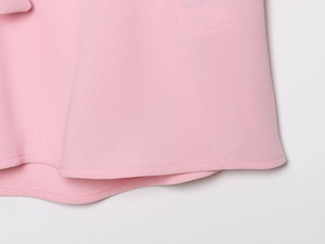 Détail de l'ourlet de la chemise rose montrant les coutures et la texture du tissu