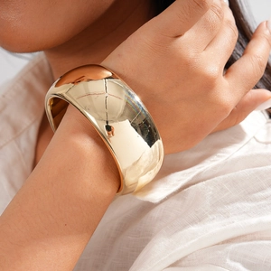 Gros plan d'un large bracelet doré poli au poignet avec une chemise blanche