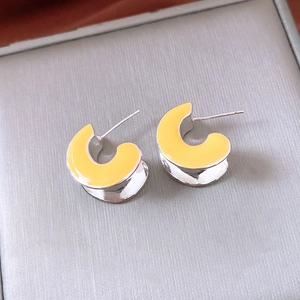 Macro detail of yellow enamel C-shaped stud earrings with polished silver metal finish
