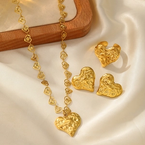 Macro view of gold heart jewelry set with matte lava texture on elegant white silk background
