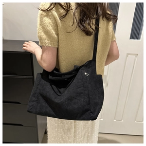 Detail of a large black corduroy tote bag worn crossbody as a stylish shoulder bag