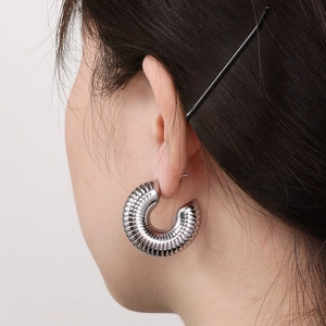 Detail of silver C-shaped hollow hoop earring with ribbed design worn by a model