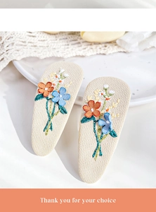 Close-up of floral embroidery on fabric hair clips featuring orange and blue flower patterns