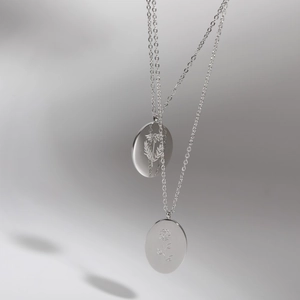 Detailed macro view of two stainless steel oval pendants with engraved flower patterns