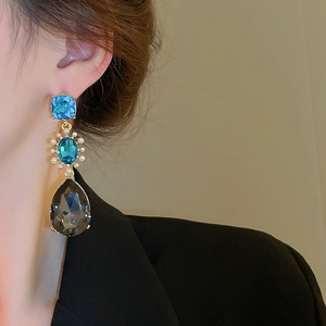 Detail of vintage gold earrings with blue gemstones and hanging grey teardrop stones