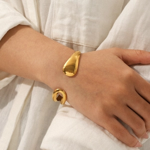 Close-up of a gold water-drop cuff bracelet with an irregular hollow design on a wrist