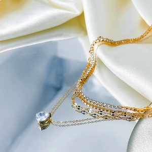 Detail of layered gold necklace with teardrop zircon pendant on elegant silk