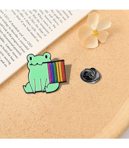 Detail of a green frog enamel pin holding a rainbow board on a warm lifestyle background