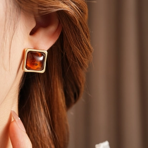 Close-up of a square amber resin earring with a gold metal frame worn by a model