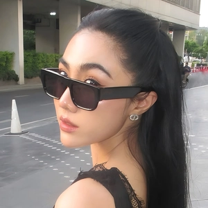 Fashionable square black sunglasses and silver cutout earrings worn by a model outdoors
