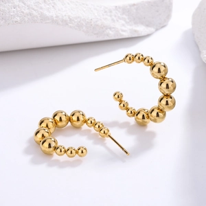 Elegant C-shaped beaded hoop earrings in gold finish on white textured stone background